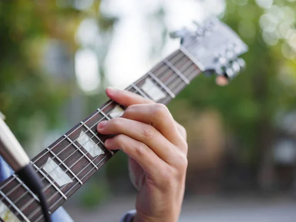 Pohled shora na mužské ruce hraje na kytaru v džínové bundy v parku na rozostřeného pozadí. — Stock fotografie