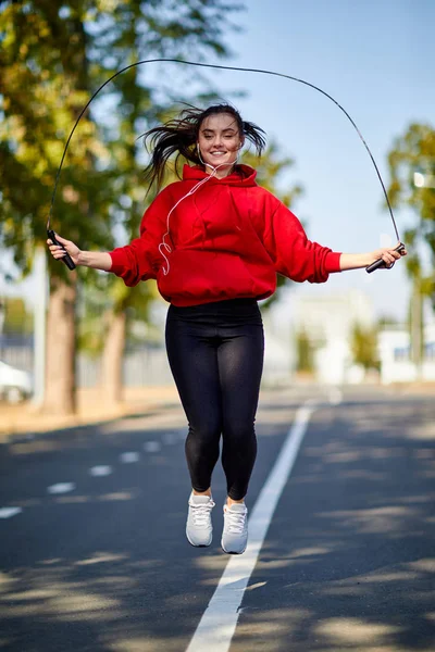 Genç gülümseyen kadın parkta ip atlıyor.