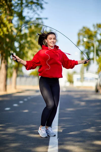 Genç gülümseyen kadın parkta ip atlıyor.