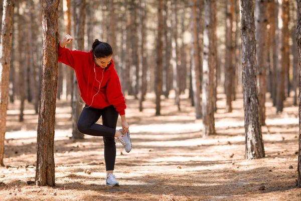 Güzel genç kız spor ayakkabı ayarlamak ağaç gövdesinde eğilir.