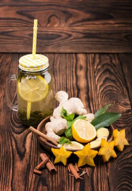Yeşil çay limon dilimi ve sarı saman ahşap zemin ile bir mason kavanoz bileşimi. Kahverengi bir plaka ile kesilmiş limon, zencefil, nane, tarçın ve bir masa üzerine carambola yıldız.