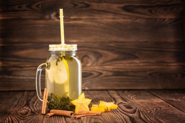 Yeşil çay limon dilimi ve sarı saman ahşap zemin ile bir mason kavanoz bileşimi. Tarçın ve carambola yıldız sıcak limonlu çay yakın. Kopya alanı.