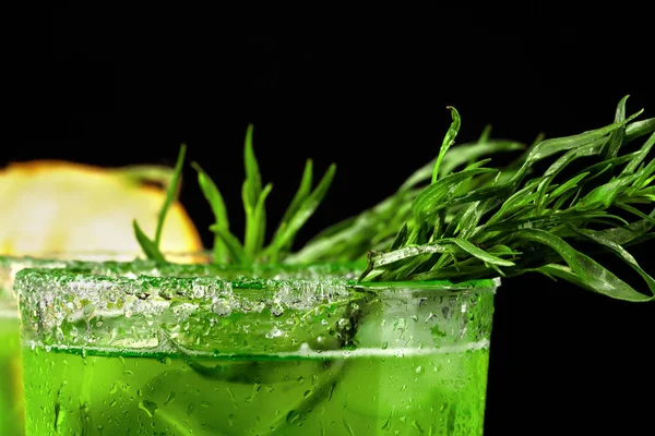 Lezzetli ve serinletici alkol içecek parlak baharatlı tarhun ve buz küpleri ile close-up. Siyah bir zemin üzerine uzun bir bardak meyveli kokteyl. Soğuk içecek ve kesme sulu kavun.