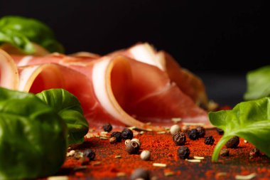 Bir kırmızı prosciutto et, yeşil ıspanak salatası ve baharatlı acı biber siyah tablo arka plan üzerinde yakın çekim bir resim. Dilimlenmiş jambon taze fesleğen ile mükemmel. Restoran meze ve geleneksel aperatifler. 