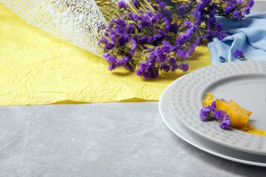 Renkli çiçek kompozisyon. Mavi ve sarı kumaş üzerinde küçük mor çiçekler buket. Süslü tabaklar gri bir arka plan masa. Sağlık, gevşeme ve romantizm kavramı.
