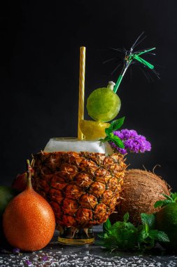 Bir büyük ananas Kupası enerjik kokteyl tam nane ve siyah bir zemin üzerine buz küpleri ile yakın çekim. Bir katı Hindistan cevizi, nane ve limon içecek yakınındaki. Egzotik meyve kompozisyonu.