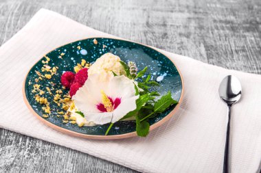 Bir tabak dolusu soğuk algınlığından ahududu, rendelenmiş ceviz ile vanilya tatlı nane beyaz bir kumaş ve ahşap arka plan. Dondurma kaşık toz bir dekoratif çiçek. Mavi plaka yakınındaki bir çay kaşığı.