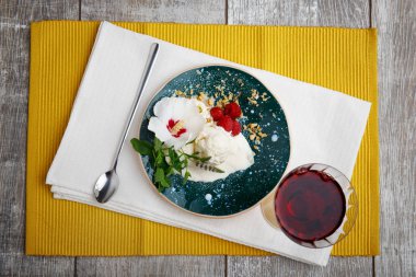 Soğuk kremalı sandviç bir görünüm yukarıdan. Mavi bir kase sütlü dondurma, rustik ahududu, baharatlı nane ve metal kaşık. Bir dondurma sarı kumaş arka plan üzerinde üzüm suyu ile. 