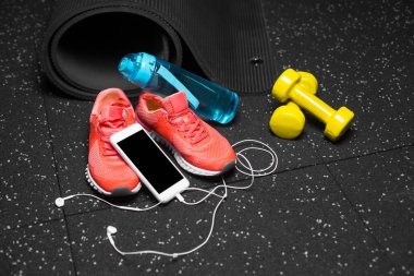 Close-Up pembe eğitim spor ayakkabı, bir şişe su, sarı dambıl, mat ve kulaklık ile smartphone bir siyah zemin arka plan üzerinde uzanan siyah. Spor ve aktivite kavramı.