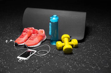 Küçük sarı dambıl, pilates mat, mavi şişe su, parlak pembe eğitmenler ve modern beyaz smartphone handphones siyah bir arka plan ile dolu. Spor ve eğitim kavramı. Kopya alanı.