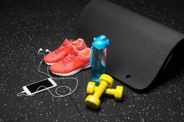 Küçük sarı dambıl, pilates mat, mavi şişe su, parlak pembe eğitmenler ve modern beyaz smartphone handphones siyah bir arka plan ile dolu. Spor ve eğitim kavramı. Kopya alanı.