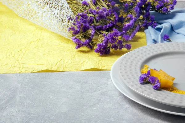 Renkli çiçek kompozisyon. Mavi ve sarı kumaş üzerinde küçük mor çiçekler buket. Süslü tabaklar gri bir arka plan masa. Sağlık, gevşeme ve romantizm kavramı.