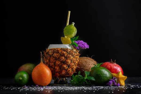 Tropik meyveler siyah tablo arka plan üzerinde renkli bir dizi. Bir bardak ananas turuncu, kahverengi Hindistan cevizi ve taze nane yanında yapılmış. Egzotik portakal ve carambola Gurmeler için. 