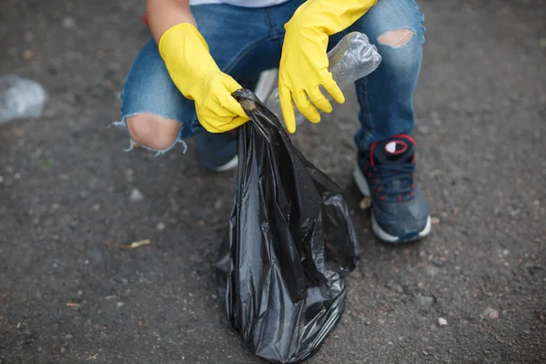 아이의 다리와 노란색 라텍스 장갑에 손을의 어린이 플라스틱 쓰레기를 따기입니다 — 스톡 사진