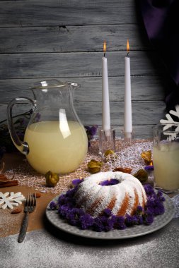 Güzel bir sofra tatil gıdalardan üstten görünüm gri bir ahşap zemin üzerinde. Buzlanma ile geleneksel ev yapımı kek ve bir plaka üzerinde dekoratif çiçek. Ananas suyu ve bir masada mumlar.