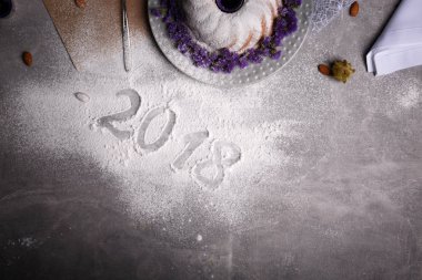 Gelen dondurulmuş tablo arka plan üzerinde şenlikli bir geleneksel Noel kek yanındaki 2018 işareti yukarıda görüntüleyin. Doğal, güzel, ev yapımı kek egzotik baharatlar ve çiçekler ile dekore edilmiştir. Kopya alanı.