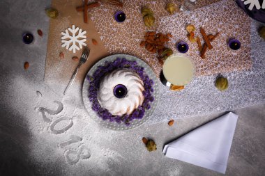 Yukarıdan görünümünü Noel yemeği bir bileşimi: badem fındık, bir bardak süt, çiçek ve kış süslemeleri yanında tarçın ile pasta. Yeni yıl 2018 işareti şenlikli bir arka plan üzerinde yazılı.