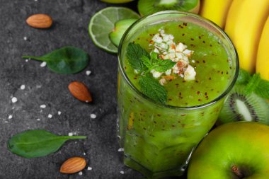 Olgun liwi ve koyu gri taş zemin üzerine rendelenmiş badem limonlu karışık bir içki close-up. Muz, Sulu kireç, olgun elma ve taze bir dalı bir masada bırakır. Organik gıda.