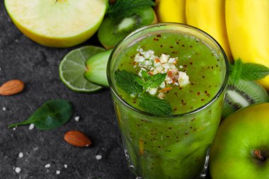 Olgun liwi ve koyu gri taş zemin üzerine rendelenmiş badem limonlu karışık bir içki close-up. Muz, Sulu kireç, olgun elma ve taze bir dalı bir masada bırakır. Organik gıda.