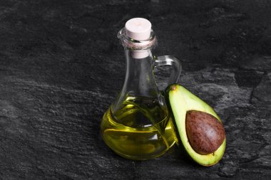 Doğal avokado yağı ve taze yeşil kesik bir koyu gri taş arka plan üzerinde avokado dolu bir cam kavanoz close-up. Organik tarımın sağlıklı çevre ürün. Kozmetik veya pişirme için malzemeler.