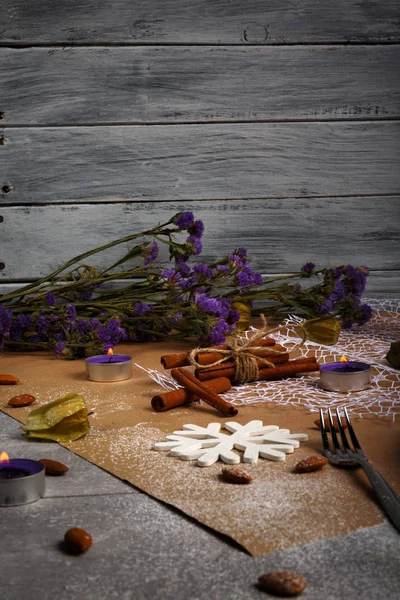 Yakın çekim resim yılbaşı süslemeleri tablo arka plan üzerinde renkli bir dizi. Baharatlı tarçın, physalis, badem fındık, şirin bir mum ve bir dekoratif kar tanesi yanında mor çiçekler. 
