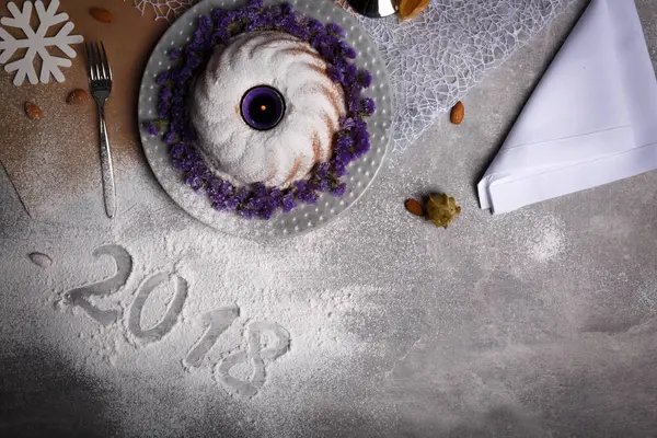 Gelen dondurulmuş tablo arka plan üzerinde şenlikli bir geleneksel Noel kek yanındaki 2018 işareti yukarıda görüntüleyin. Doğal, güzel, ev yapımı kek egzotik baharatlar ve çiçekler ile dekore edilmiştir. Kopya alanı.