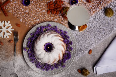 Kahverengi ve gri kumaş arka plan üzerinde güzel bir yeni yıl kompozisyon bir görünümünü yukarıda. Buzlanma ile geleneksel ev yapımı kek ve bir plaka üzerinde dekoratif çiçek. Kış içki ve bir masa üzerine badem.