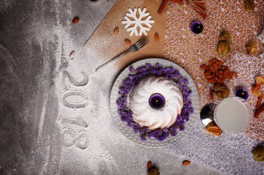 Pişmiş pasta Menekşe çiçek ve mum bir merkezindeki Noel tatili için en iyi görünümü renkli arka plan üzerinde. Bir içecek, doğal badem ve kar tanesi üzerinde gri bir tablo yığını. Kopya alanı.