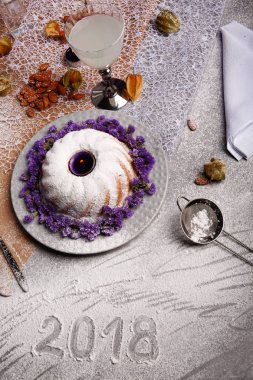 Yukarıdan bir Noel pudingi ile pudra şekeri serpilir ve açık gri renkli çiçekler ile dekore edilmiştir. Bir tatil 's kek, Hindistan cevizi sütü ve bir tablo üzerinde bir elek. Yılbaşı Dekorasyonu. 