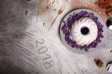 Pişmiş pasta Menekşe çiçek ve mum bir merkezindeki Noel tatili için en iyi görünümü renkli arka plan üzerinde. Bir yığın doğal badem ve kar tanesi üzerinde gri bir tablo. Kopya alanı.