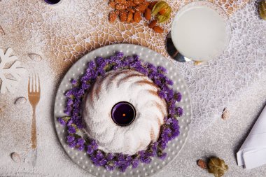 Yukarıdan bir kompozisyon bir geleneksel Noel Pasta krema ve mor çiçekler etrafında bir plaka ve renkli arka plan üzerinde pişmiş yemek. Bir Hindistan cevizi içecek ve bir yığın bir masa üzerine badem.