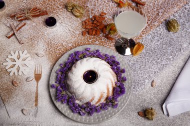 Yukarıdan bir kompozisyon bir geleneksel Noel Pasta krema ve mor çiçekler etrafında bir plaka ve renkli arka plan üzerinde pişmiş yemek. Bir Hindistan cevizi içecek ve bir yığın bir masa üzerine badem.