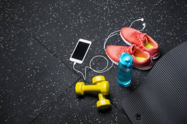 Siyah bir arka plan üzerinde yukarıdan görünüm sarı dambıl, mat, mavi şişe su, parlak pembe eğitmenler ve modern beyaz smartphone handphones ile dolu. Spor ve eğitim kavramı. Kopya alanı.