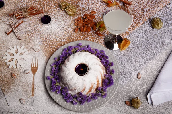Yukarıdan bir kompozisyon bir geleneksel Noel Pasta krema ve mor çiçekler etrafında bir plaka ve renkli arka plan üzerinde pişmiş yemek. Bir Hindistan cevizi içecek ve bir yığın bir masa üzerine badem.
