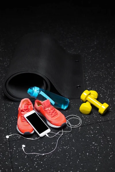 Mavi bir şişe su, mat, parlak pembe Eğitim ayakkabı, fiziksel egzersizler ve modern telefon handphones ile sarı araçlar germe benekli bir siyah arka plan üzerine siyah yakın çekim resim.