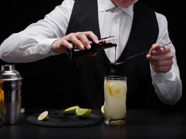 Zarif, şık bir profesyonel ekipman için siyah arka plan üzerine sallar barmenle. Uzun boylu kalın suyu bir bardak ıhlamur ve buz ile alkollü meyveli içecek dökülen bir barmen Close-Up.