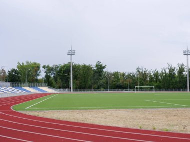 Bir futbol sahası ve eğitimler ve yarışmalar bir yeşil doğal arka plan üzerinde çalıştırmak için kırmızı bir parça ile bir yaz stadyum. Spor, açık havada, yaz, futbol kavramı. Kopya alanı.