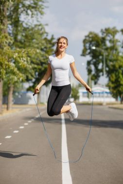 Athletic young woman training with a jumping rope on a park background. Gymnastics equipment concept. clipart