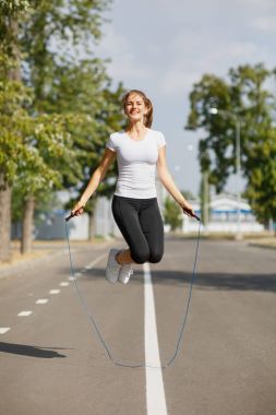 Park arka plan üzerinde ip atlama ile eğitim atletik genç kadın. Jimnastik cihazları kavramı.