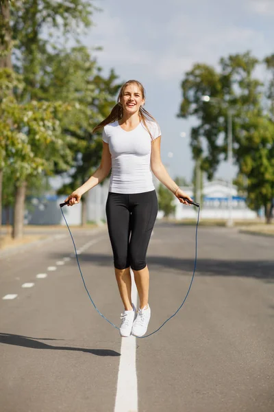 Athletic young woman training with a jumping rope on a park background. Gymnastics equipment concept.