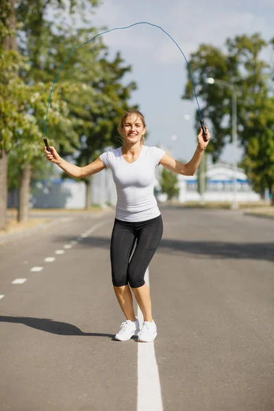 Park arka plan üzerinde ip atlama ile eğitim atletik genç kadın. Jimnastik cihazları kavramı.