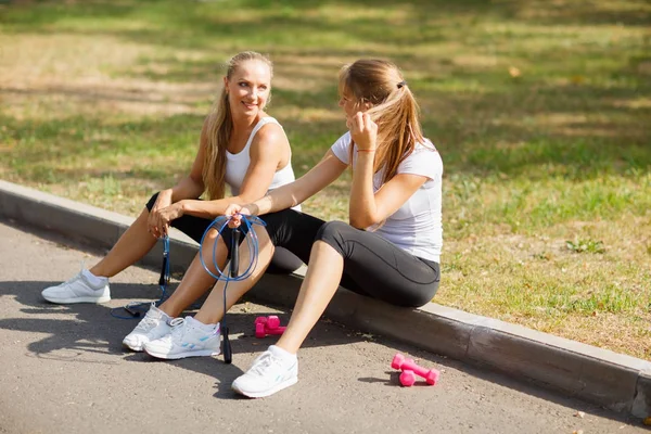 Doğal bir arka plan üzerinde eğitimden sonra su ile oturan gülümseyen güzel kızlar. Rahatlatıcı spor kavramı. — Stok fotoğraf