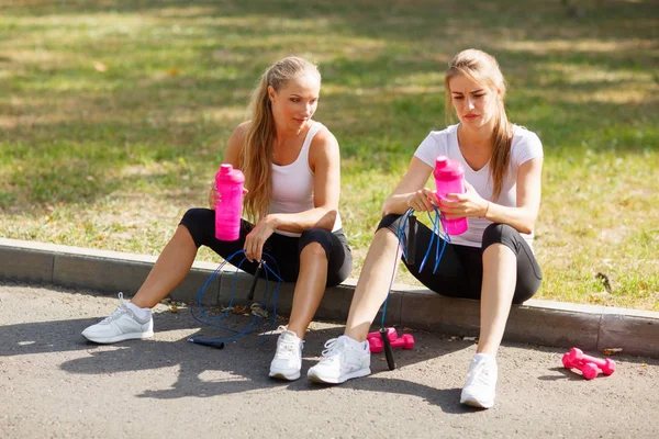 Doğal bir arka plan üzerinde eğitimden sonra su ile oturan gülümseyen güzel kızlar. Rahatlatıcı spor kavramı. — Stok fotoğraf