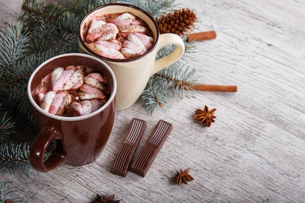 Two cups of sweet cocoa with marshmallows next to a pine branch on a table background. Winter hot chocolate. — Stock Photo, Image