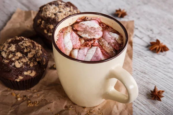 Hot chocolate with marshmallows and cupcakes on a table background. Coffee and muffins. Winter cafe desserts. — Stock Photo, Image