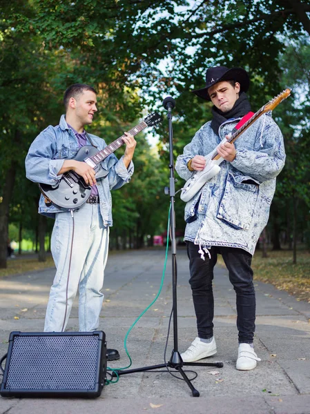 Happy young guys sings songs and plays guitar on a jeans jacket in a park on a natural background.