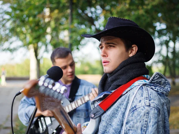 Young guy sings songs and plays guitar on a jeans jacket in a park on a natural background. Music concept.