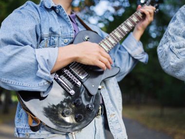 Genç adam şarkı söylüyor ve doğal bir arka plan üzerinde bir parkta bir kot ceket gitar çalar. Müzik konsepti.