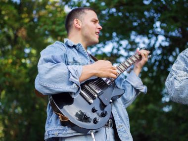 Genç adam şarkı söylüyor ve doğal bir arka plan üzerinde bir parkta bir kot ceket gitar çalar. Müzik konsepti.