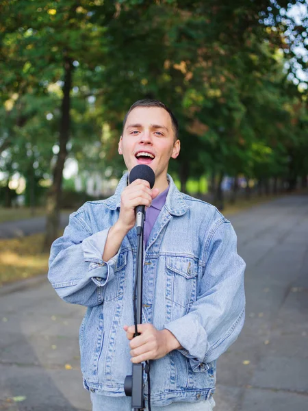 Young guy sings songs and plays guitar on a jeans jacket in a park on a natural background.